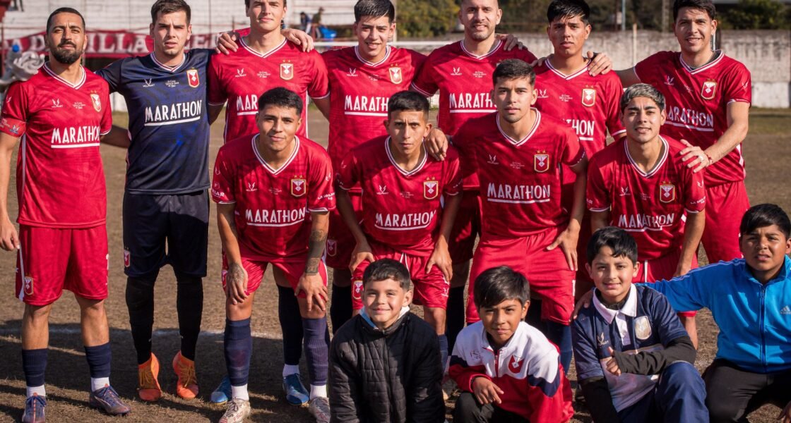 Formación titular de Tucumán Central posando para la foto grupal antes del partido, vistiendo camisetas rojas junto al arquero en azul y tres niños arrodillados adelante.